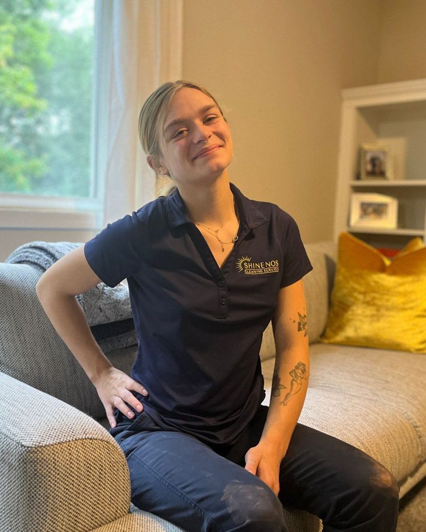 Smiling Shinenos house cleaner in navy uniform relaxing on a client's sofa after a clean